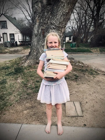 Young reader holding huge stack of books, very excited to read.